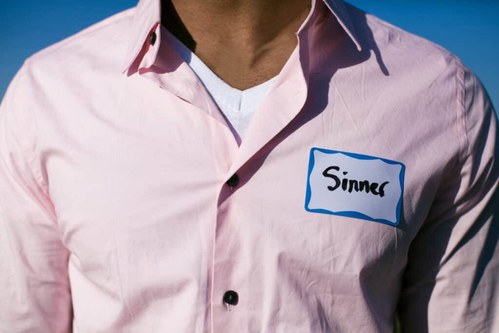 Man wearing pink dress shirt with a name tag that reads, "sinner". 