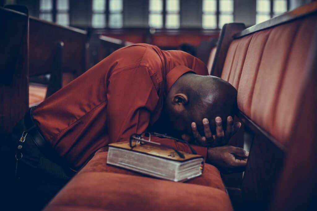 Man kneeling in a church pew with bowed in prayer.