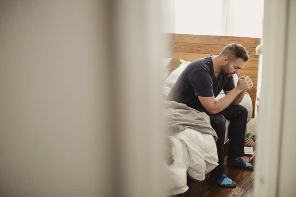 Man sitting on the edge of bed praying. 