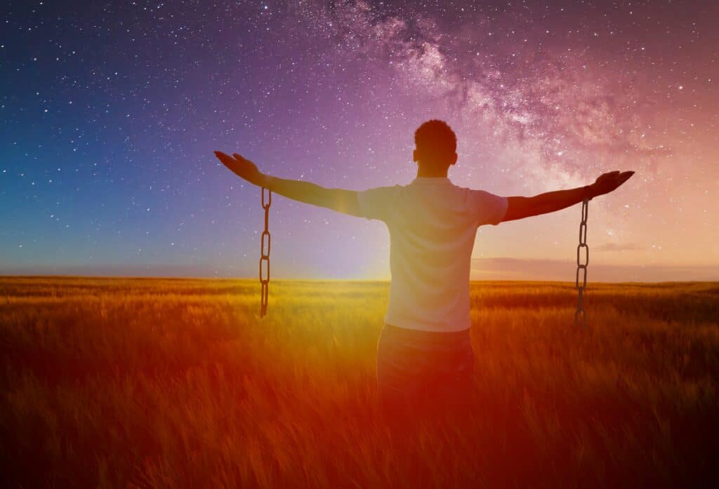 Man standing in a field, with arms raised and chains hanging off the arms.