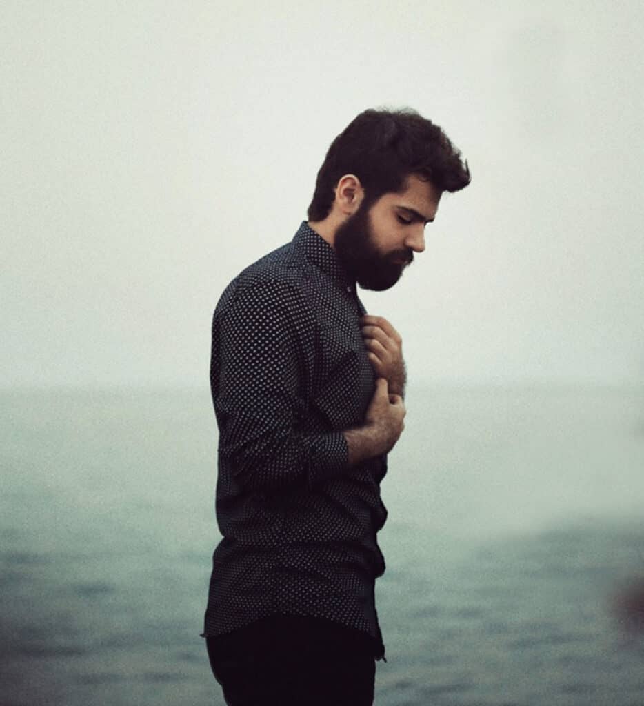 Man standing in front of the ocean with hands on his chest. 