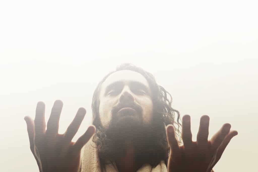 Man with hands raised palm up in front of face.