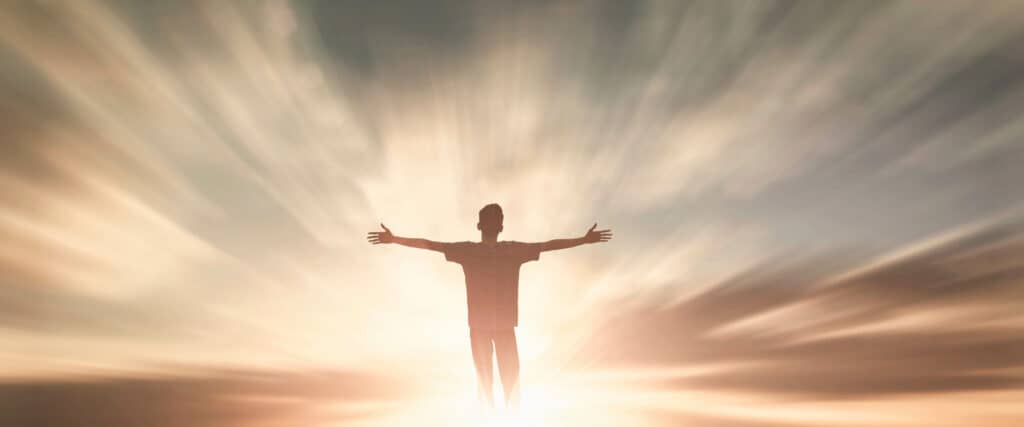 Man silhouetted by the sun with arms raised.