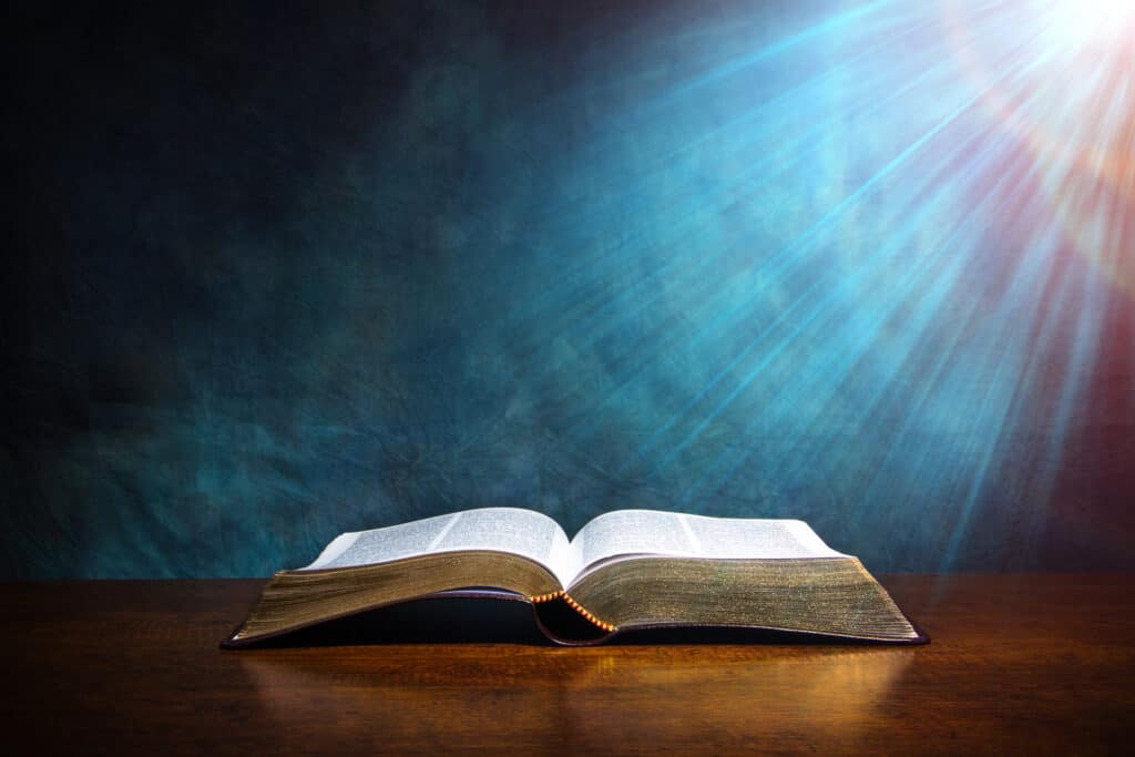 Bible open on table and sun shining down.