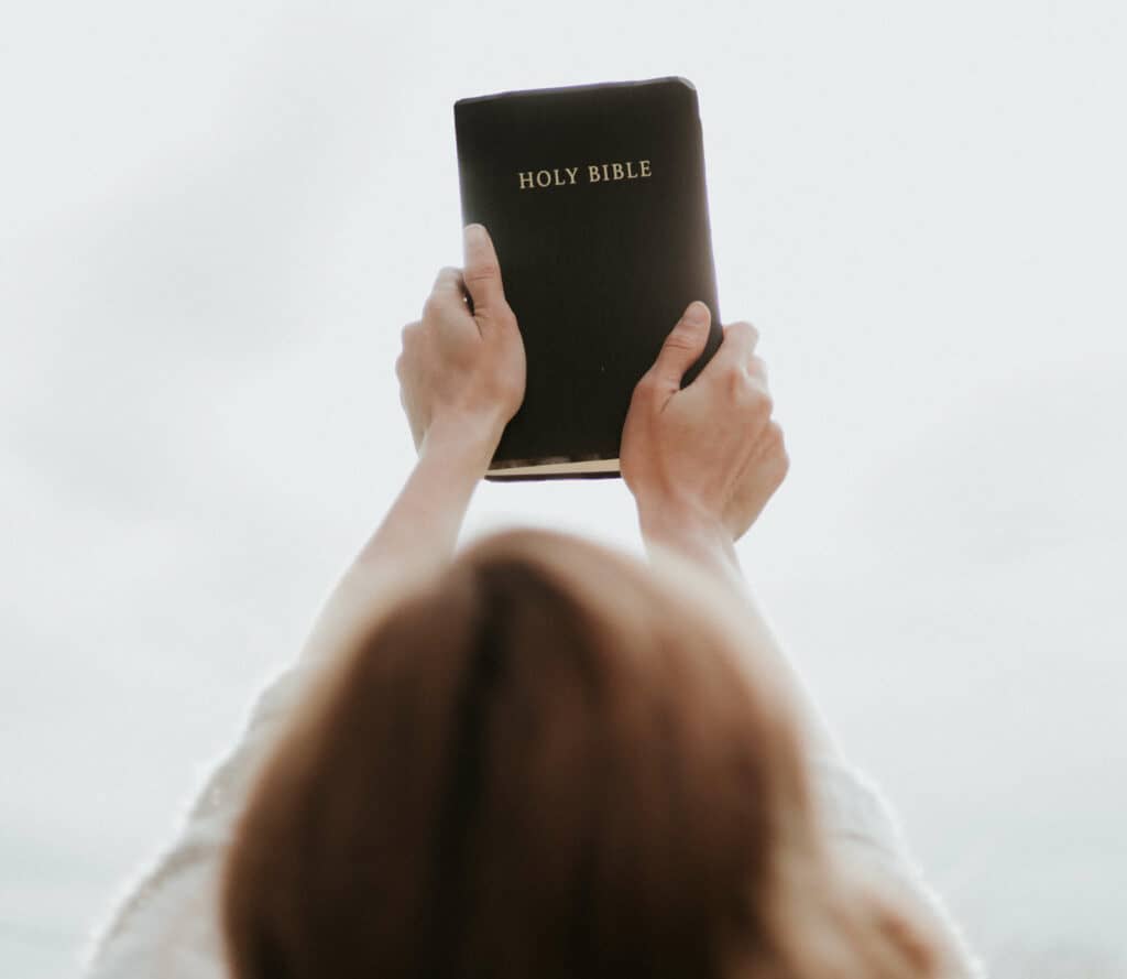 Person holding bible with two hands stretched out in front of them.