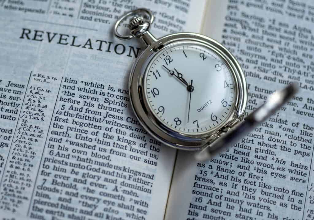 Pocket watch laying open on a Bible that is open to revelation.