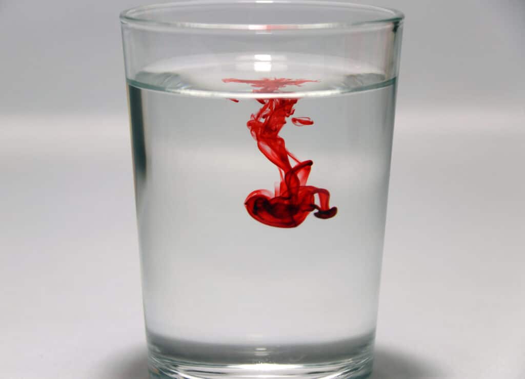 A red drop of ink in a clear glass of water. 