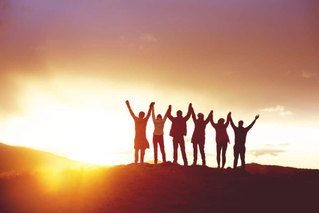 A group of people lined up with their hands raised while the sun sets.
