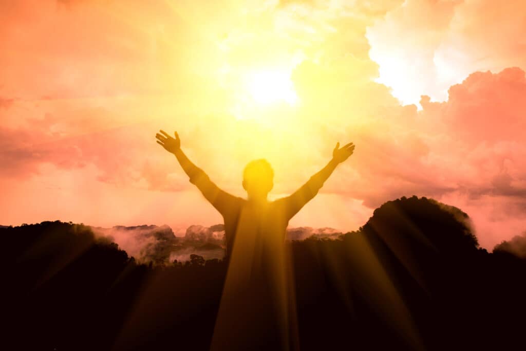 Hands raised in praise with the sun shining on the individual.