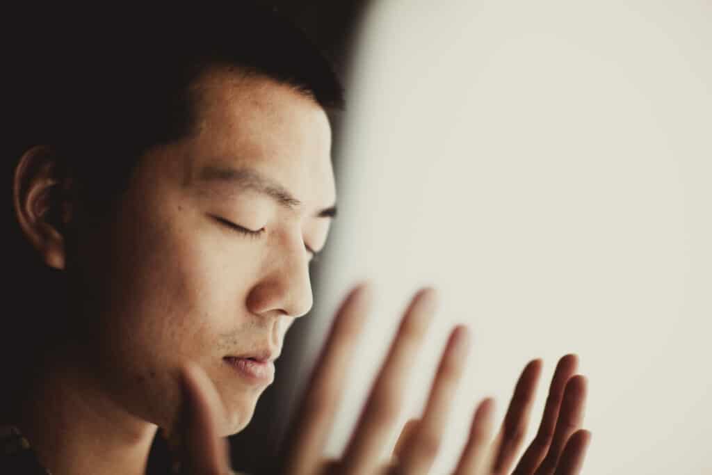Man with eyes closed and hands raised near face.