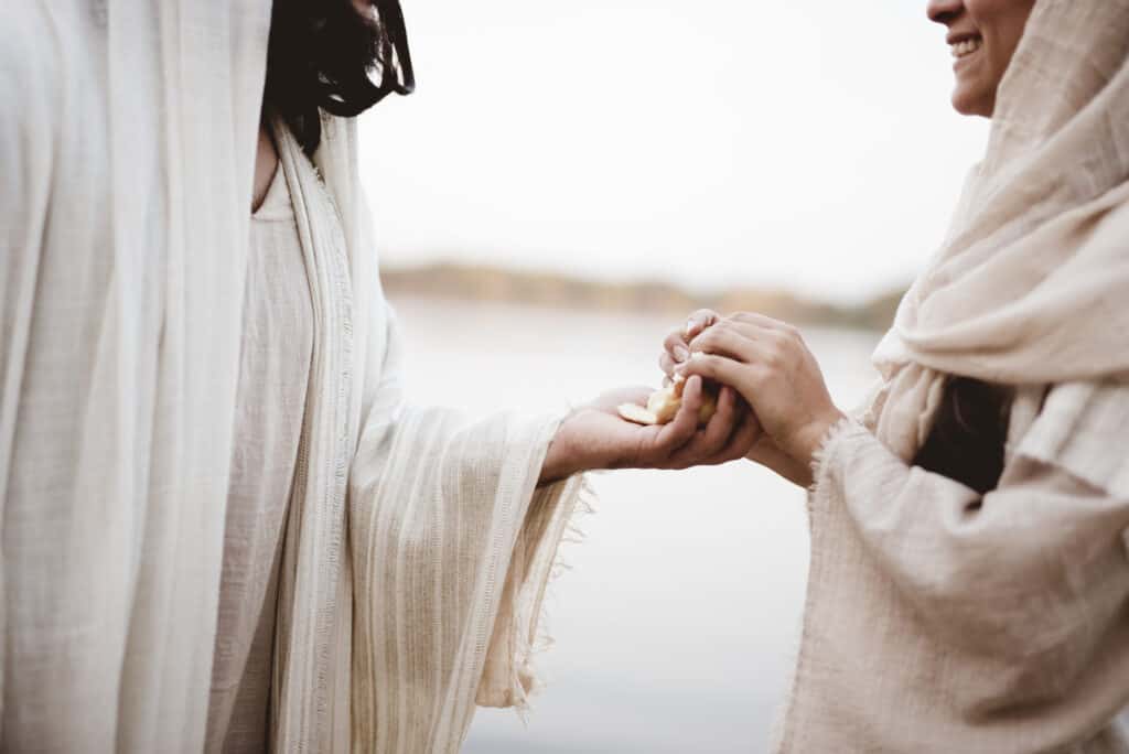 Person giving a piece of bread to another person. 