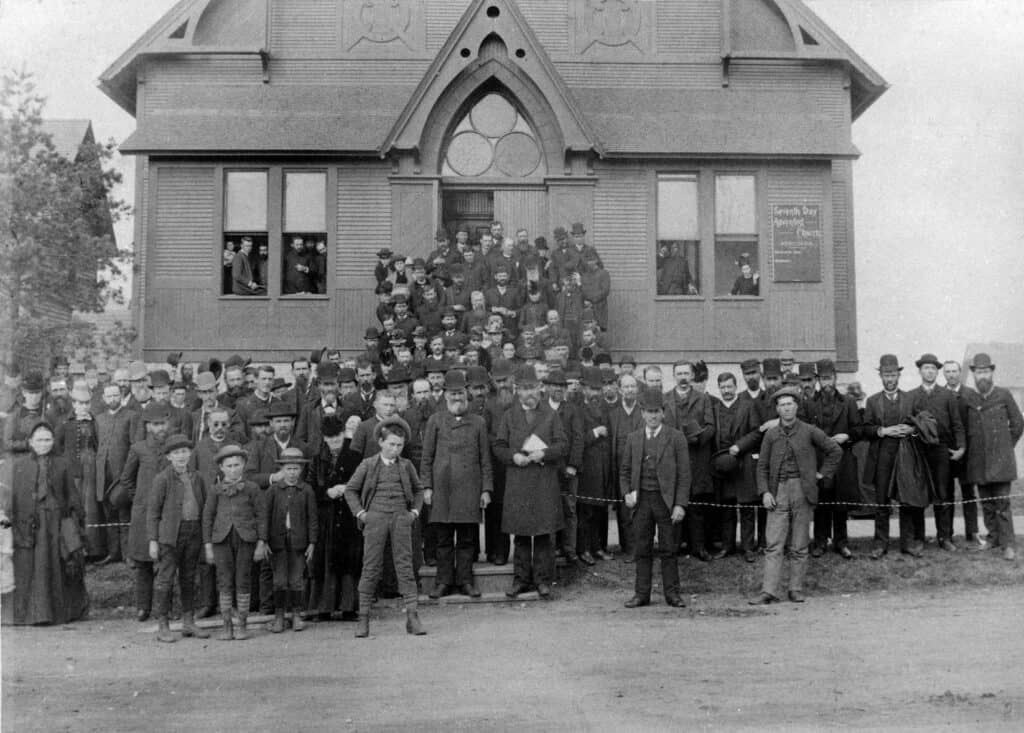 An early Seventh-day Adventist Church members crowded in front of their church and on the stairs together.