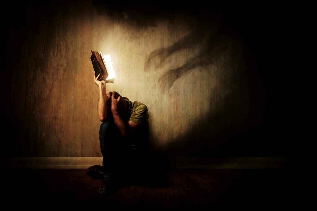 Man fighting off evil shadows pressing in around him by holding up the Bible shining light of good.