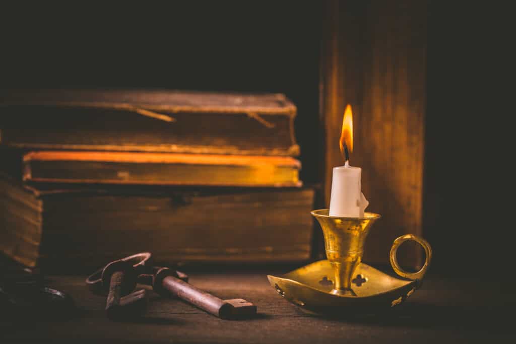 A candle lit shining in the dark next to a key and Bible, in a similar setting to how the Waldenses had to copy the Bible by hand.