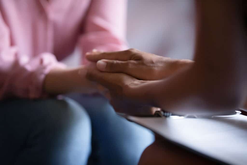 Two women holding hands as they pray for each other.