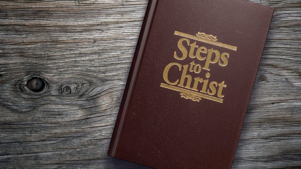 Ellen White's book 'Steps to Christ' laying on a wood table.