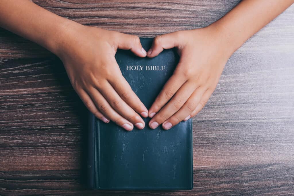 Two hands forming a heart around the Holy Bible, in a symbol of love for God.