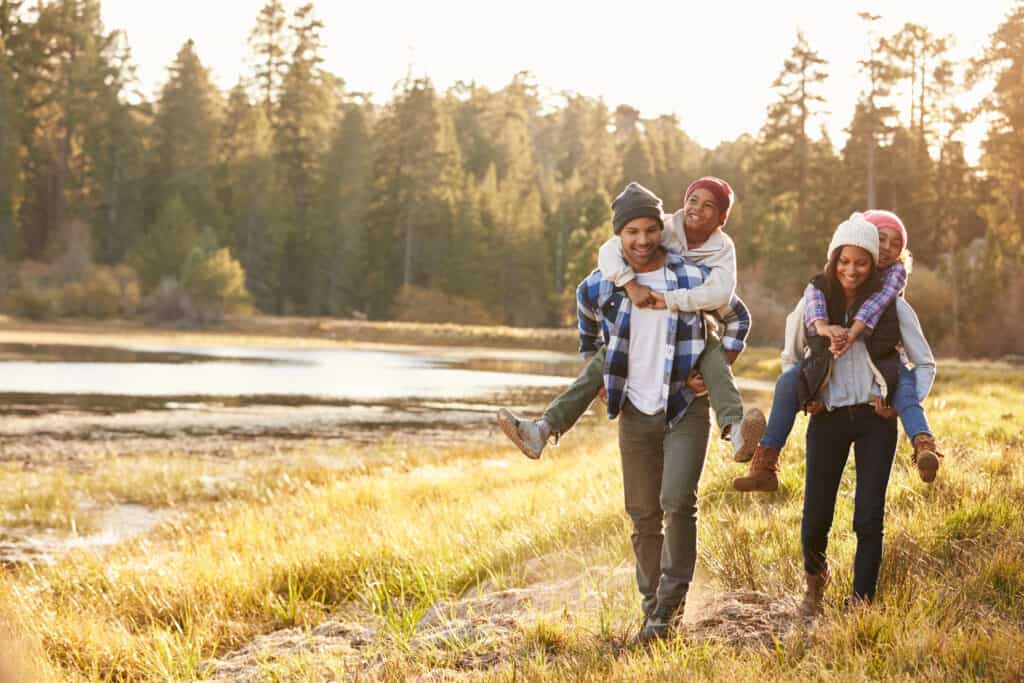 Parents giving their two daughters piggyback rides while they get clean fresh air and exercise outside.