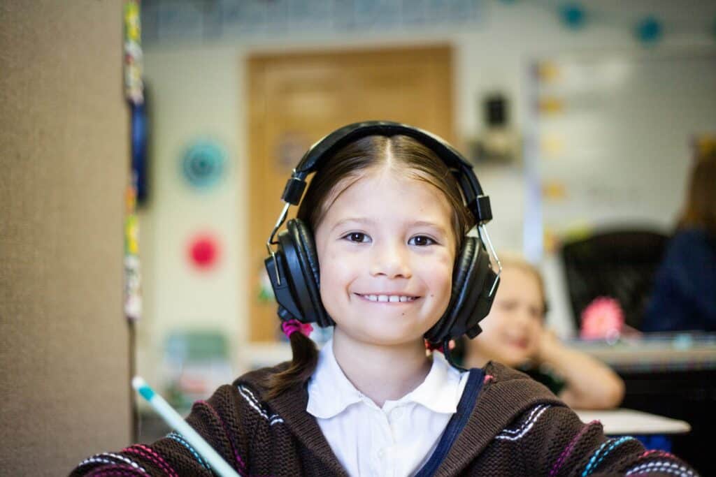 Young girl smiling, listening through a headset in her classes special curriculum.