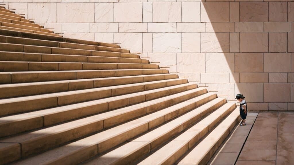 Toddler looking at the small steps in front of them leading to a large flight of stairs.