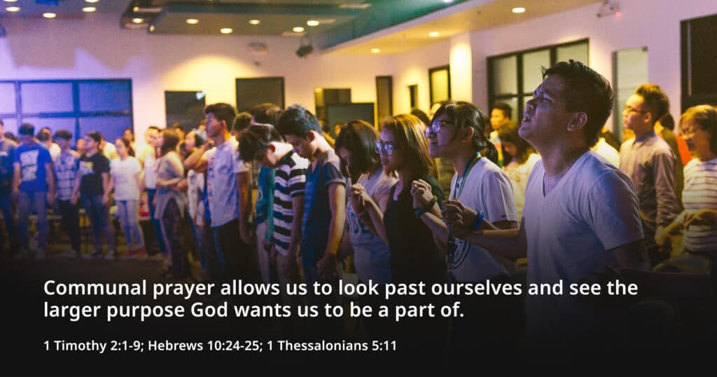 Communal prayer of a community of youth in a fellowship hall linking hands together.