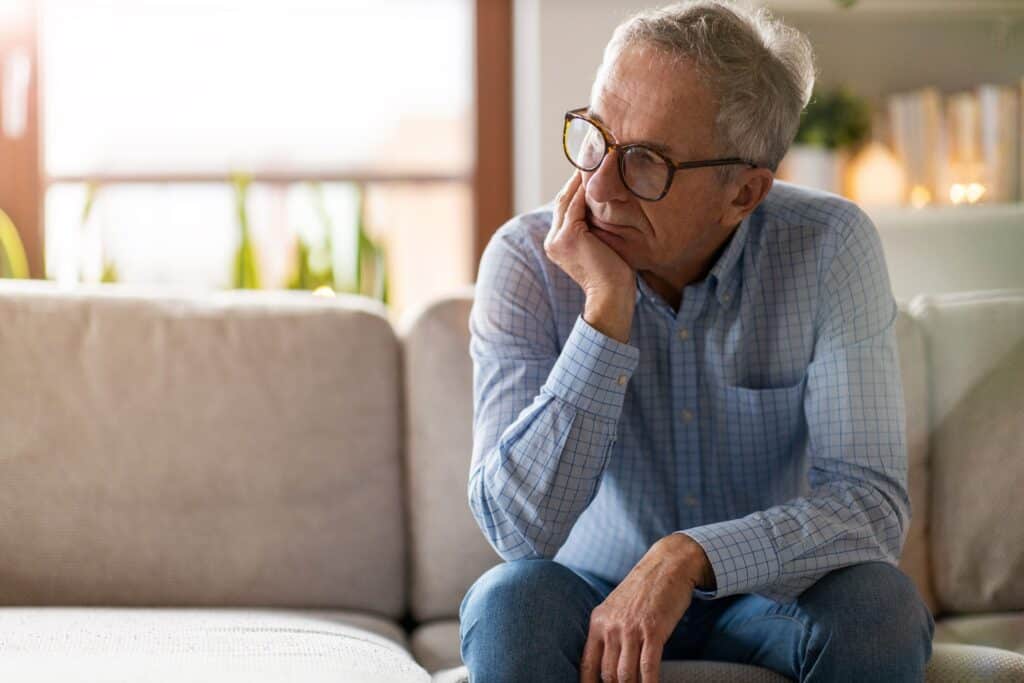 An older man leaning on his hand as he sits on a couch thinking about God.