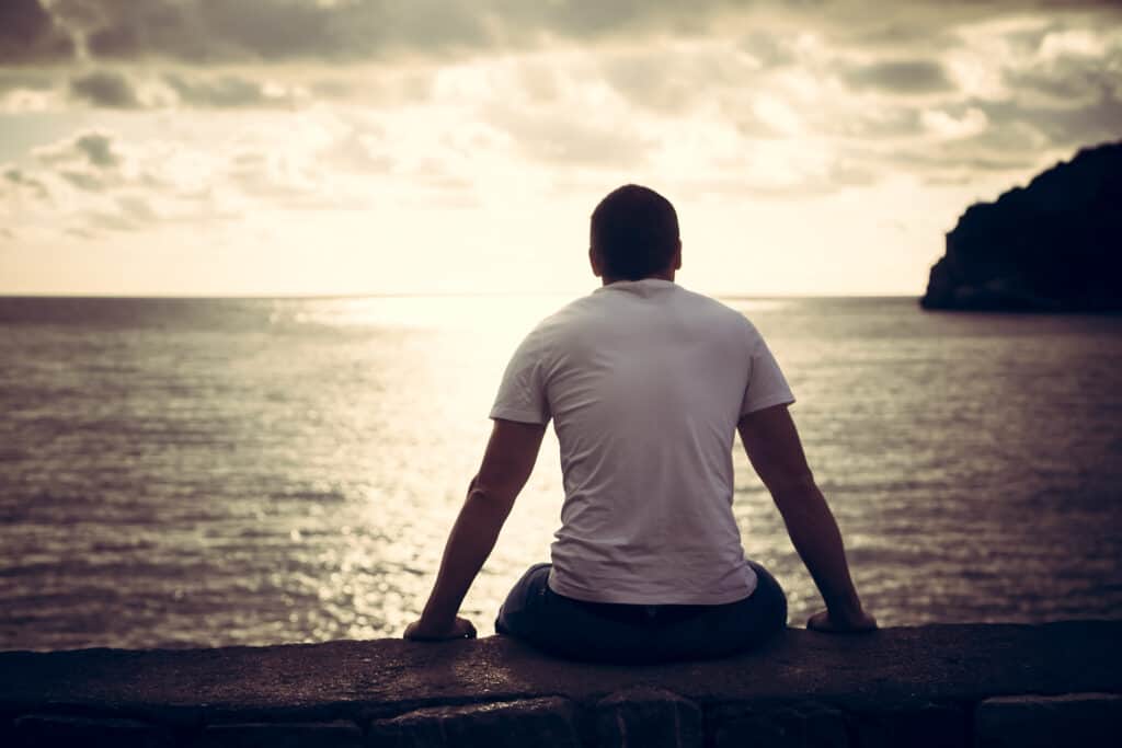 Young man sitting on a pier looking out over a lake.