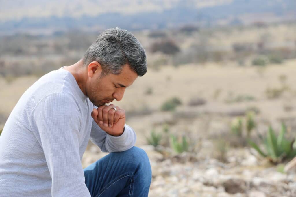 Man kneeling in prayer outside in the desert.
