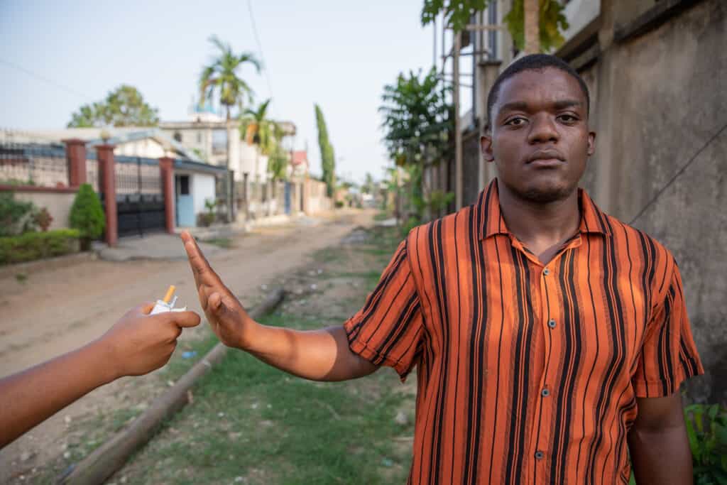 A man holds up his hand, saying no to someone offering him a cigarette in an act of practicing self-control.
