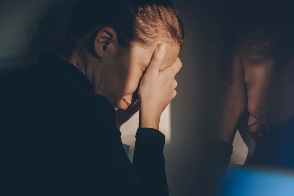 Woman holding her face up against a window in despair.