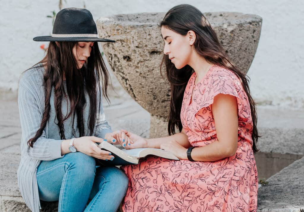 Two sisters praying together over a Bible, supporting each other.