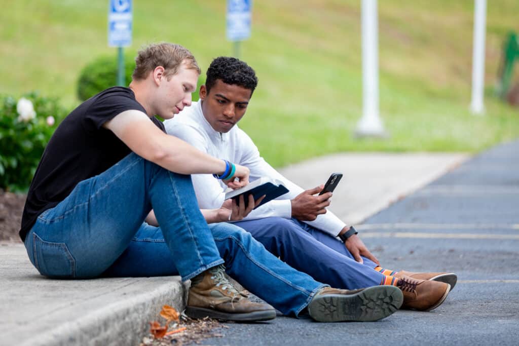 Sharing the Bible Two men sitting on a sidewalk as one man shows the other a Bible verse.