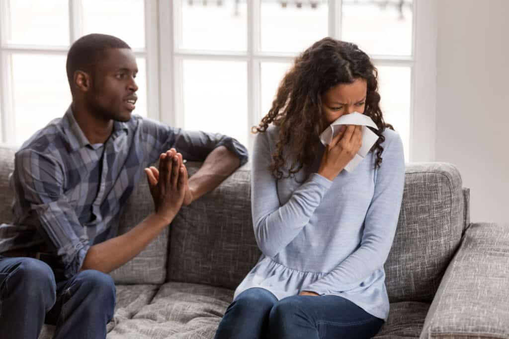 A woman crying into a tissue as her husband asks for forgiveness.