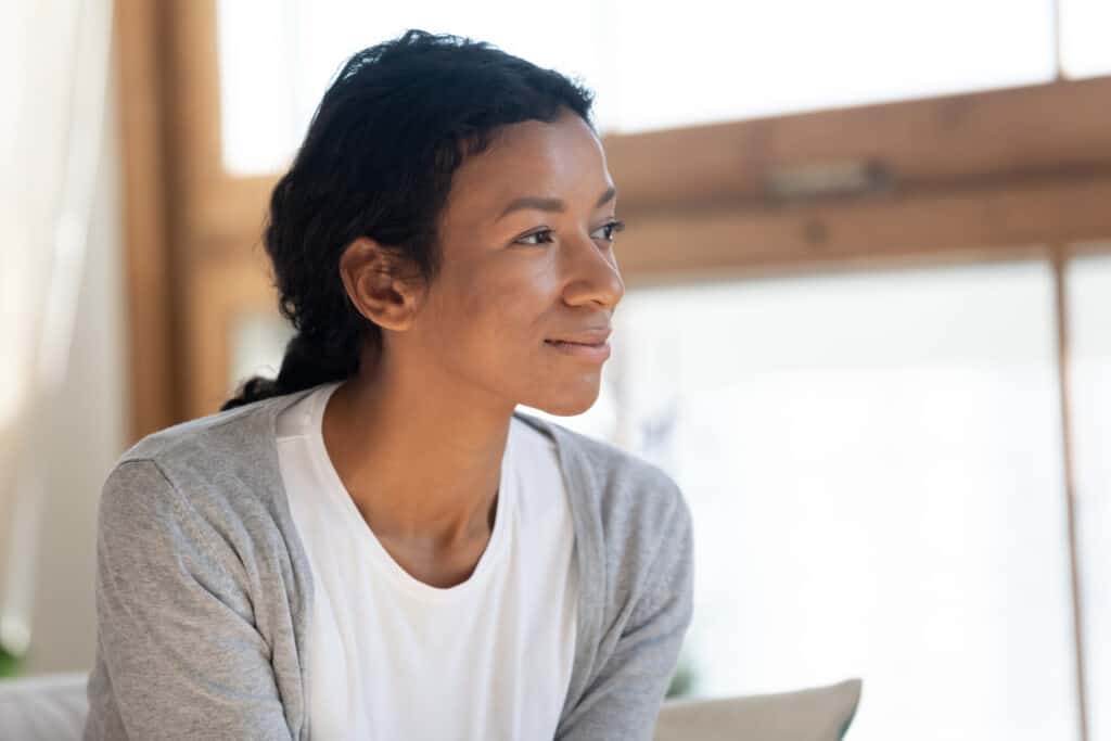 Young woman smiles while sitting on a chair thinking about how God has helped her transform.