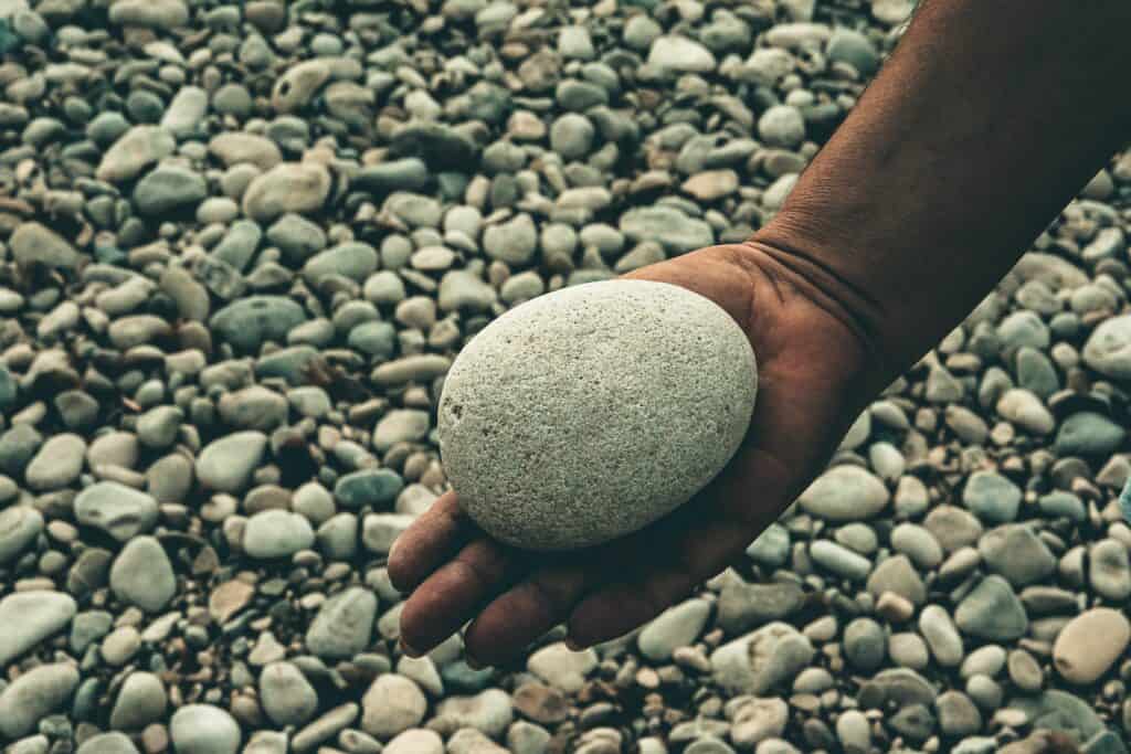A hand holding a stone in a gravel pit, similar to where Stephen was stoned in Acts 7.