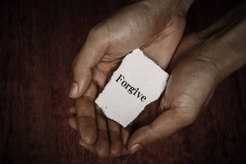 A persons hands holding a rough cut stone with the word forgive engraved on it.