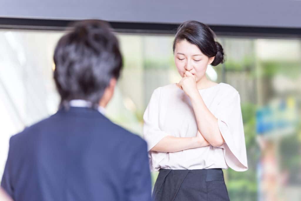 A woman stands with her eyes closed thinking, as her husband waits for her answer after apologizing.