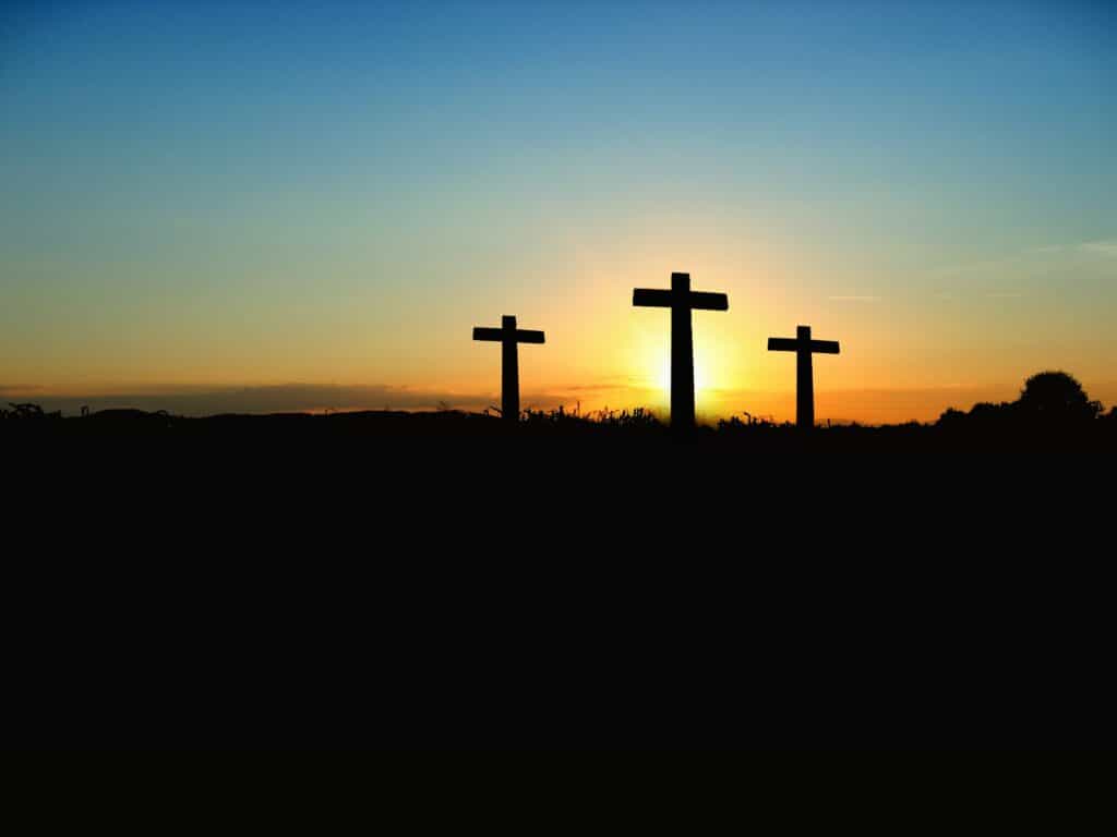 Silhouette of the three crosses on the hill, as the sun sets in the background.